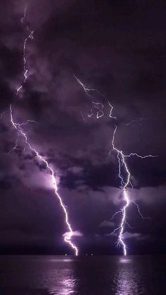 a lightning bolt is seen over the ocean at night with dark clouds and bright lights