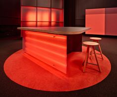 an empty bar with stools in front of it and red lighting on the wall