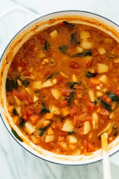 a pot filled with vegetable soup on top of a white counter next to a wooden spoon