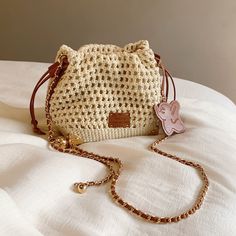 a white purse sitting on top of a bed next to a gold chain bracelet and a pink butterfly brooch