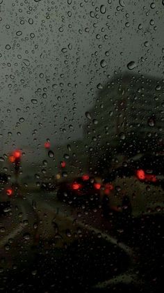 rain drops on the windshield of a car as traffic lights are seen in the background