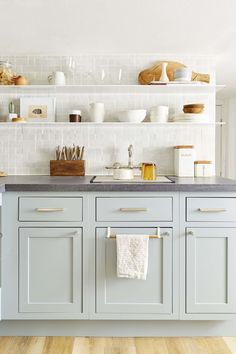 a kitchen with white cabinets and gray counter tops is pictured in this image, there are dishes on the shelves above the sink