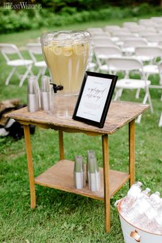 a wooden table topped with bottles and glasses next to a white bucket filled with drinks