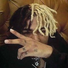 a man with dreadlocks making the v sign while sitting in a chair holding his hand up to his face