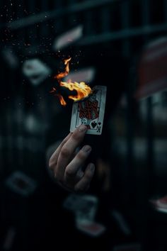 a person holding up a burning playing card