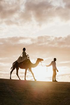 two people are walking with a camel in the desert at sunset or sunrise, while the sun is low to the ground