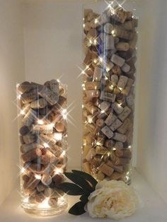 two vases filled with wine corks next to a white rose and some lights