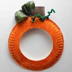 a paper plate shaped like a pumpkin with green leaves on it and a piece of cardboard sticking out of the top