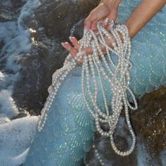 a woman is holding pearls in her hand while sitting on the rocks at the beach