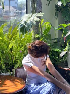 a woman sitting on a bench in front of some plants