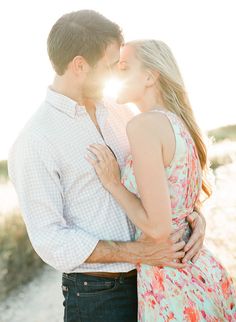 a man and woman kissing in front of the sun with their arms around each other