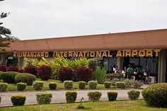 people are walking in front of an airport terminal with many bushes and trees around it