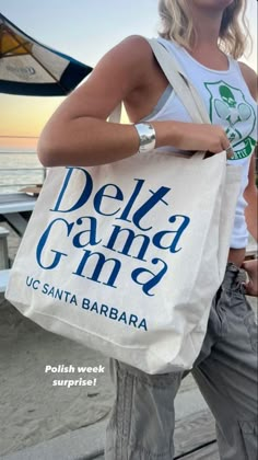 a woman standing on the beach holding a bag