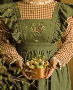 a woman wearing an apron holding a bowl of fruit