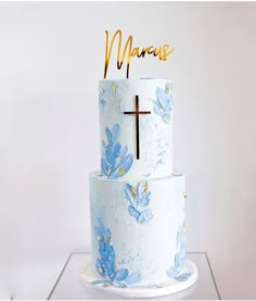 a three tiered cake with blue flowers and a cross on top that says marques