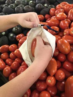 someone is picking up some tomatoes and avocados from the bin at the market