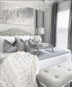 a white bed sitting under a chandelier next to a window