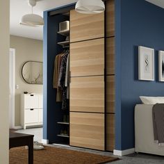 an open closet with clothes hanging on the door and drawers in it, next to a bed