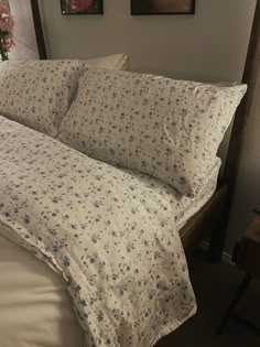 a bed with white sheets and blue flowers on the comforter is next to two framed pictures