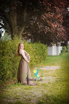 a woman in a long dress is posing for a photo by some bushes and trees