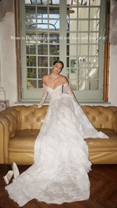 a woman in a white wedding dress sitting on a brown leather couch next to a window