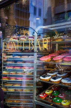 a woman standing in front of a donut shop with lots of doughnuts