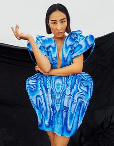 a woman in a blue dress is posing for the camera with her arms folded out