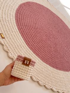 a hand holding a crocheted rug on top of a white table with pink accents