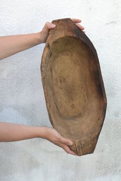 a person holding a wooden bowl with their hands on the top of it, against a white wall