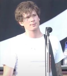 a young man standing in front of a microphone and wearing a white t - shirt