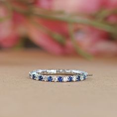 a blue and white diamond ring sitting on top of a wooden table next to flowers