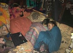 two women sitting on a couch covered in blankets with laptops and papers all over them