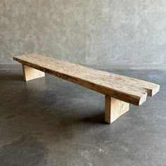 a wooden bench sitting on top of a cement floor in front of a gray wall