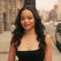 a woman in a black dress is standing on the sidewalk and smiling at the camera