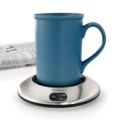 a blue coffee cup sitting on top of a saucer with a black base and silver trim