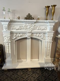 a white fireplace with two gold vases on top of it and a black carpet