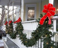 christmas wreaths on the front porch decorated with red bows and lights are hanging from the railing