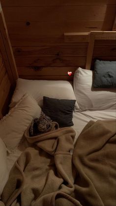 an unmade bed with pillows and blankets on it in a room that has wood paneling