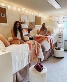 two women sitting on twin beds in a room with white walls and carpeted flooring