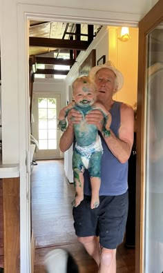 an older man holding a baby in his arms while walking into a house with another dog