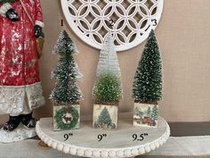 three small christmas trees sitting on top of a white shelf next to a clock and other decorations