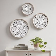 three decorative white plates mounted on the wall above a table with a potted plant