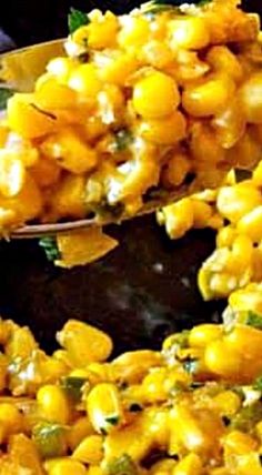 a spoon filled with corn and peas on top of a black plate next to other food items