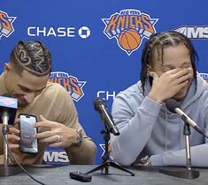 two people sitting at a table in front of microphones with their hands covering their faces