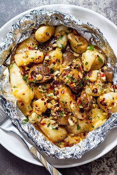 an aluminum foil covered dish with potatoes and mushrooms in it on a plate next to a fork