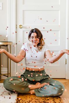 a woman sitting on the floor with confetti falling from her hands in front of her