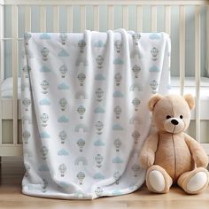 a teddy bear sitting next to a crib with a blanket on top of it