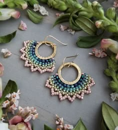 a pair of earrings sitting on top of a table next to flowers and greenery