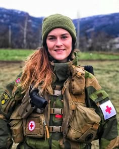 a woman in camouflage is smiling at the camera while wearing a green hat and jacket with red cross patches on it