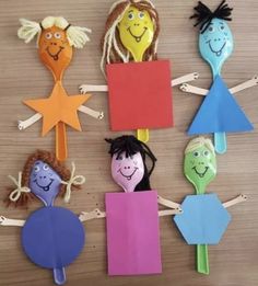 paper puppets with faces and hair hanging from clothes pins on a wooden table in the shape of children's heads